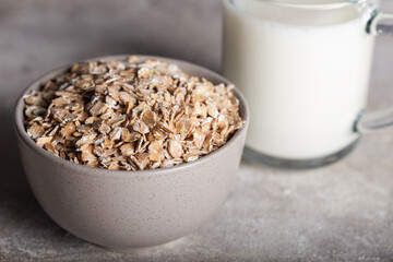 Rye flakes in a round wooden bowl with glass of milk on a stone background. Healthy cereal flakes in a ceramic bowl and milk close-up.