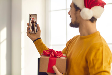 Young man in Santa hat video calling friends who are having fun at Christmas party