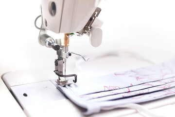 An industrial high-speed sewing machine sews an individual protective cotton face mask with screen print in bright light - sustainable pandemic fashion concept