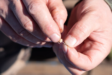 Male hands put a larva bait on a fish hook close up selective focus