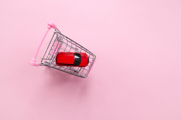 Red toy car in a shopping cart on a pastel pink background, top view, copy space. The concept of buying a car online, a gift for Valentine's Day, women's shopping, leasing services. Horizontal