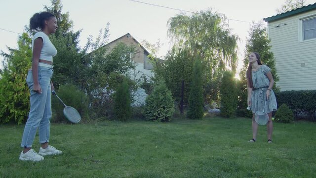 Two Young Women Play Badminton On A Green Lawn In The Backyard Of Their Home