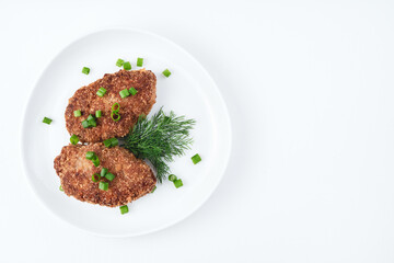 Two juicy cutlets are sprinkled with green onions and dill in a white plate on a light background. Top view with space to copy. The concept of cooking.