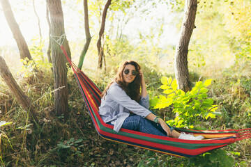 Young beautiful girl resting in a colored hammock in the park and reading a book