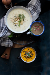 Three bowls of different soups: asparagus, carrots and pumpkin and mushrooms over a rustic and elegant background.