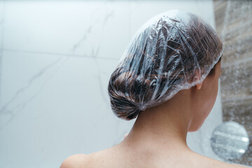 Back view. Woman puts a shower cap on her hair