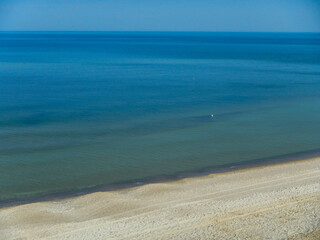 A view of a very calm sea with no waves and the beach and the breakwater.