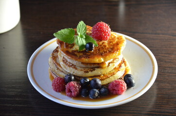 Pancakes with berries and maple syrup with raspberries and blueberries on a black background