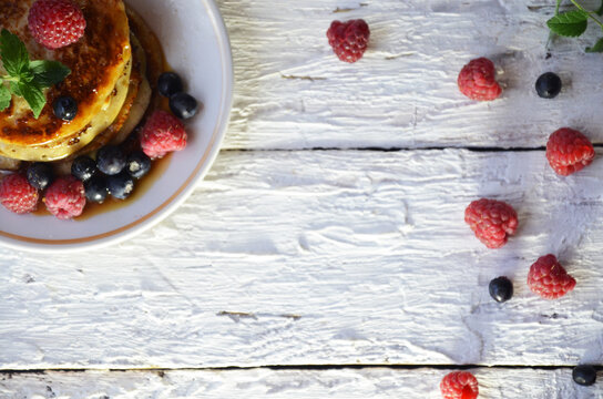 Pancakes with berries and maple syrup in a plate on a white wooden background