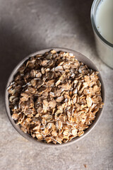 Rye flakes in a bowl with glass of milk on a stone background. Healthy cereal flakes in a ceramic bowl and milk close-up.
