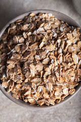 Healthy cereal flakes in a ceramic bowl. Rye flakes in a bowl on stone background. Top view.