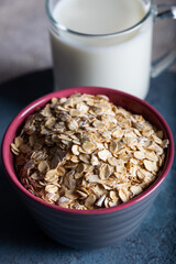 Dry rolled oatmeal in a bowl with milk on dark blue background. Healthy cereal flakes in a ceramic bowl and glass of milk close-up.
