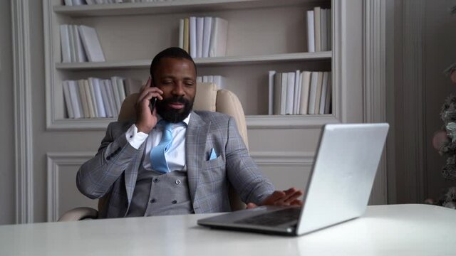 confident black guy is sitting in office and talking by cell phone, successful and rich entrepreneur