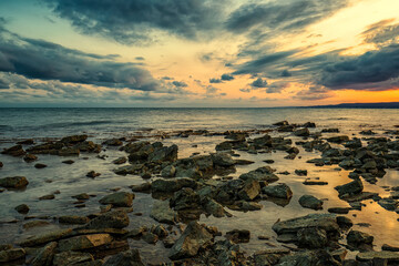 Obraz premium Stone beach at sunset. Twilight sea and sky. Dramatic sky and clouds. Nature landscape.