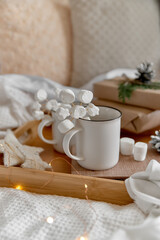 Fototapeta na wymiar Hot cocoa with marshmallow in a white ceramic mug, on a wooden tray and wrapped boxes. The concept of cosy holidays and New Year. Selective focus