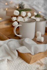 Hot cocoa with marshmallow in a white ceramic mug,  on a wooden tray and wrapped boxes. The concept of cosy holidays and New Year. Selective focus