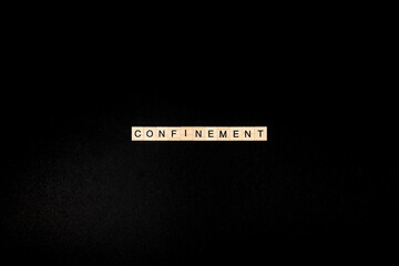 Wooden letters on a black background forming the word “confinement”. Second wave during Coronavirus pandemic concept.