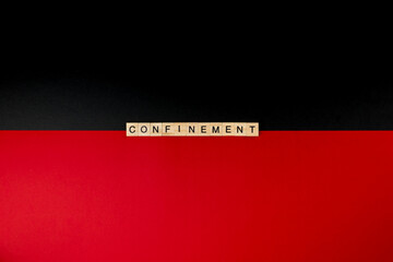 Wooden letters on a red and black background forming the word “confinement”. Second wave during Coronavirus pandemic concept.