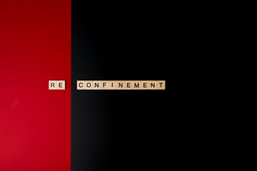 Wooden letters on a red and black background forming the word “reconfinement”. Second wave during Coronavirus pandemic concept.