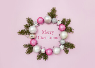 Phrase Merry Christmas and decorative wreath of pink and silver balls and spruce branches. New year greeting card template.