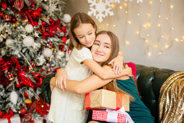 Fototapeta na wymiar Two happy sisters aged eight and fifteen exchange gifts in a beautiful Christmas interior