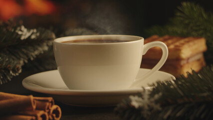 White cup of hot coffee on a brown wooden table. Green spruce branches, homemade waffles with souffle and cinnamon. Christmas lights on background. Cozy atmosphere. New Year and Christmas concept