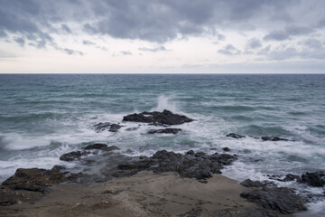 Fototapeta na wymiar Seascape on a cloudy day with strong waves breaking against the rocks.