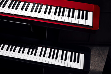 Fototapeta premium Electronic synthesizers (piano keyboards) close-up shot with dark background. Beautiful red and black musical keyboards with balck and white keys. Modern, minimalistic look, top view.