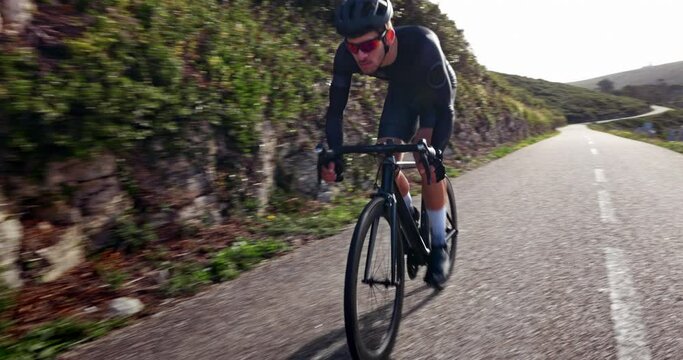 Male cyclist riding sports bicycle fast uphill on mountain road