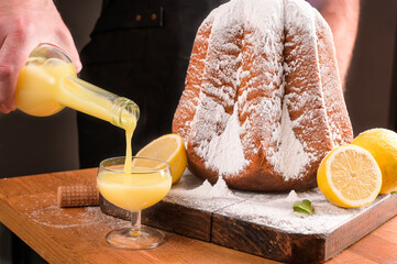 Man pours Limoncello in a glass on the table and a soft star-shaped pasta sprinkled with icing...