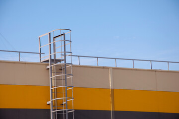 Fototapeta premium Modern beige, yellow and dark grey house with metal staircase on the blue sky background.