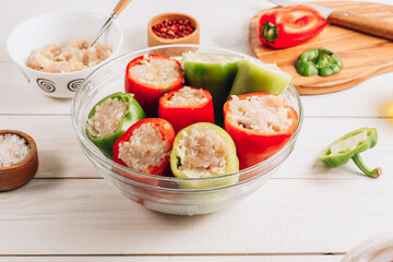 Pepper stuffed with chicken minced meat and rice in a glass bowl on a white wooden background.