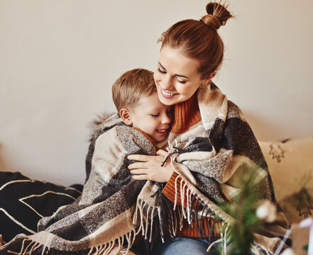 happy family mother and loving son hug and laugh wrapped in a warm blanket on a cozy winter evening at home .