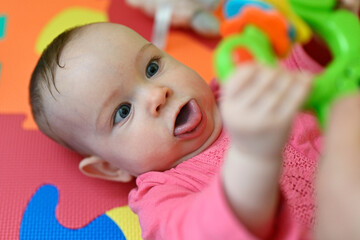 Seven month old baby girl lying on her back and holding a rattle.