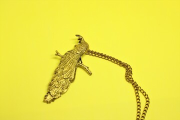 A Golden color or golden plated Peacock or peafowl necklace or locket on golden chain isolated on yellow background 