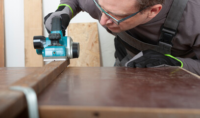 Carpenter working with  electric planer on wood lath on desk, on background oriented strand board