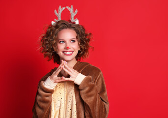 cute funny young woman in a Christmas reindeer costume smiles and rejoices on colorful red background.