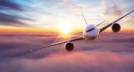 Commercial airplane flying above clouds in dramatic sunset light.