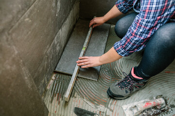 Unrecognizable female bricklayer checking the floor with a level to install a tile floor