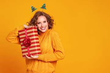 cheerful surprised   woman  smiling and holds a Christmas gift on a colored yellow background.