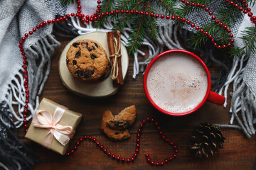Festive, holiday Christmas concept. Cozy winter home background with cookies, hot cocoa drink, Christmas tree branches, blanket and gift. Top view, selective focus