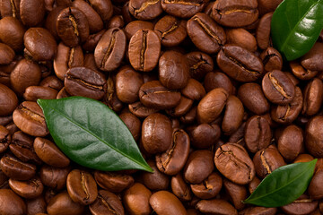 roasted coffee beans with green leaves background. Top view. Close Up.

