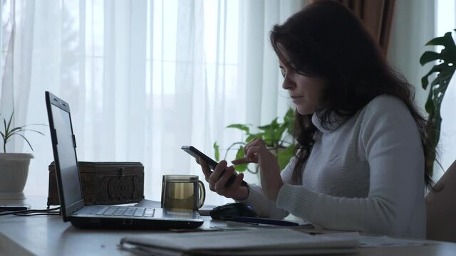 Woman Calculates Expenses on Smartphone Counting Money Dollar Cash while Working Bills Taxes Planning Family Budget. Serious Housewife at Office Table. Evening at Home. 2x Slow motion 60 fps 4K
