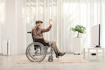Elderly disabled man waving from a wheelchair in front of a tv