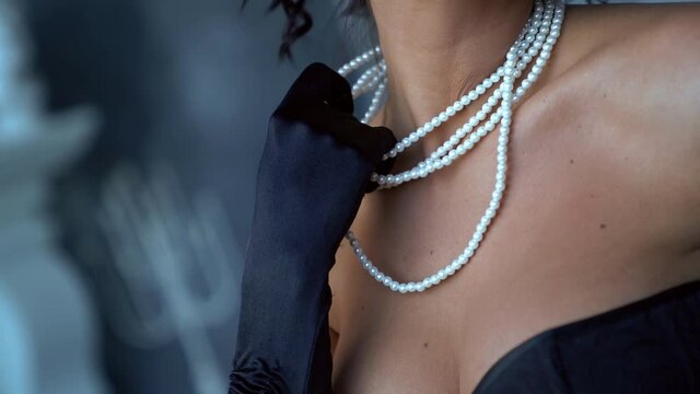 seductive brunette woman is playing with her expensive pearl necklace and smiling broadly, closeup