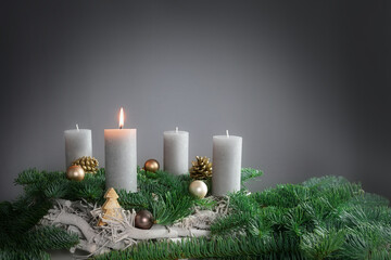 One of four candles is burning for the first Advent on fir branches with Christmas decoration...