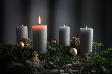 Four candles, one of them lit on an advent arrangement from fir branches and Christmas ornaments,...