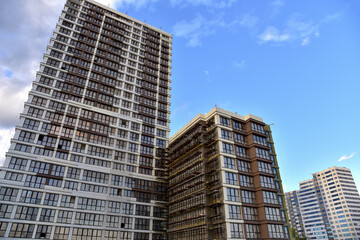 Scaffolding used in construction new building. Facade of a new modern high-rise residential building. Skyscraper on blue sky background. Tall house renovation project, government programs.