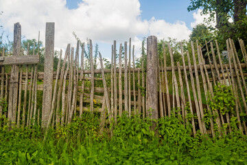 Fototapeta premium Old rickety wooden fence made of narrow boards in front of village house