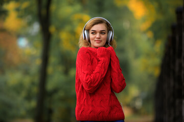 Happy woman in red pullover listening music through headphones in the autumn park